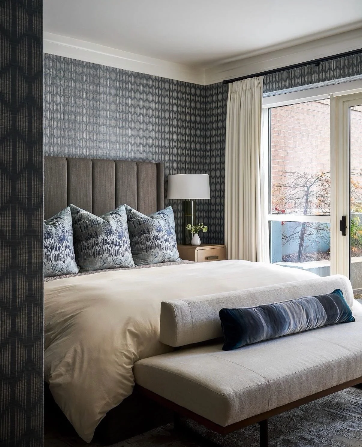 Layer upon layer, this primary bedroom reveals its character through thoughtful details. Textural wallcoverings, tailored upholstery, warm wood tones, and subtle pattern play work in harmony to create depth, comfort, and quiet sophistication. Every e