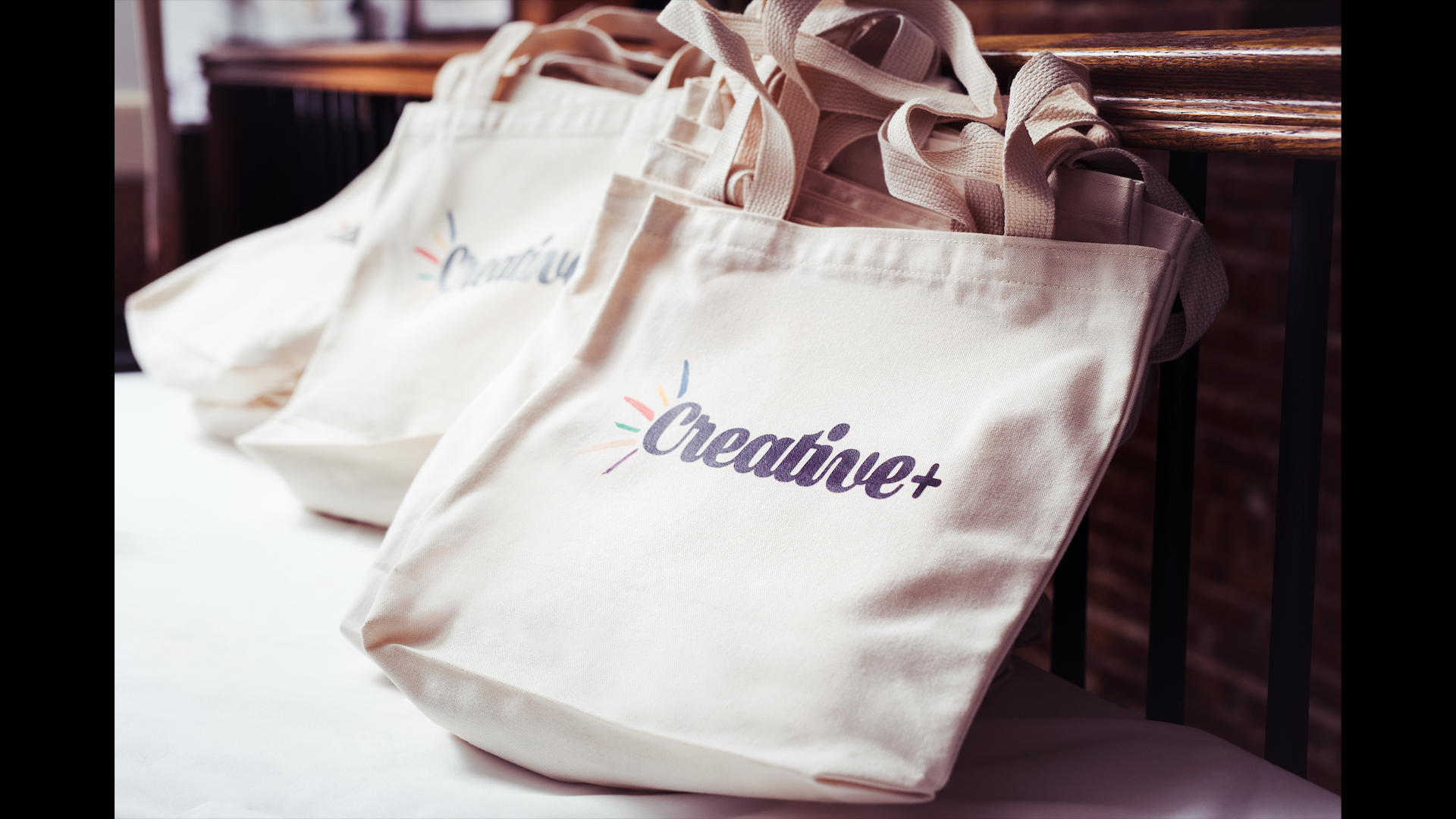 Cream-colored tote bags with the word 'Creative' printed on them, hanging on a wooden and metal railing.