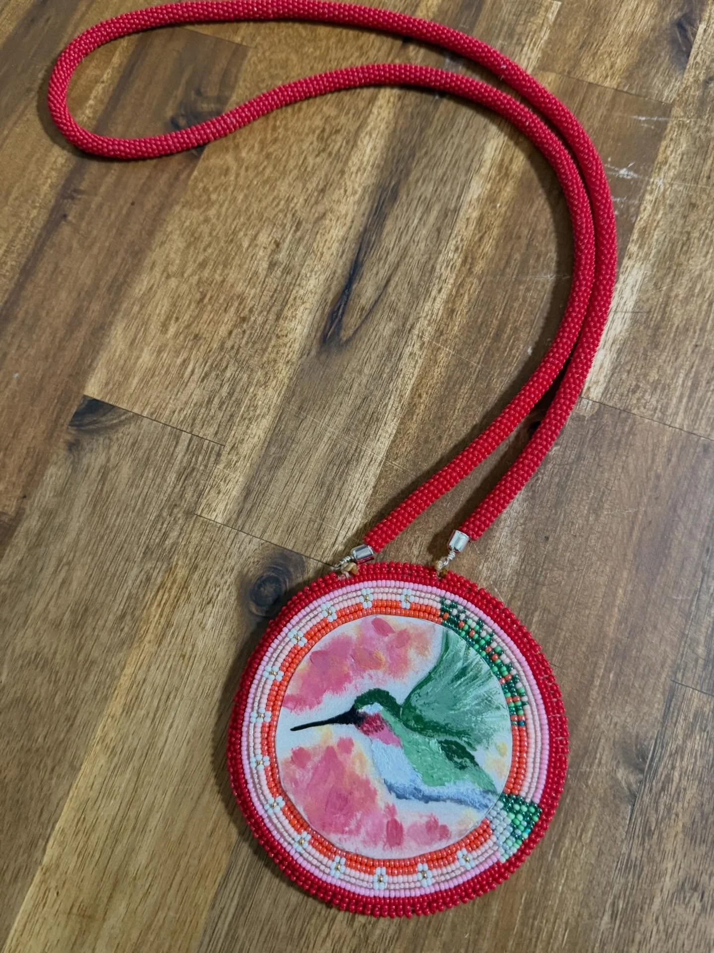 This medallion is hand painted on rawhide and beaded with buckskin backing. This is available on our  website February 1st! #beadedmedallion #valentinesjewelry #indigenousart