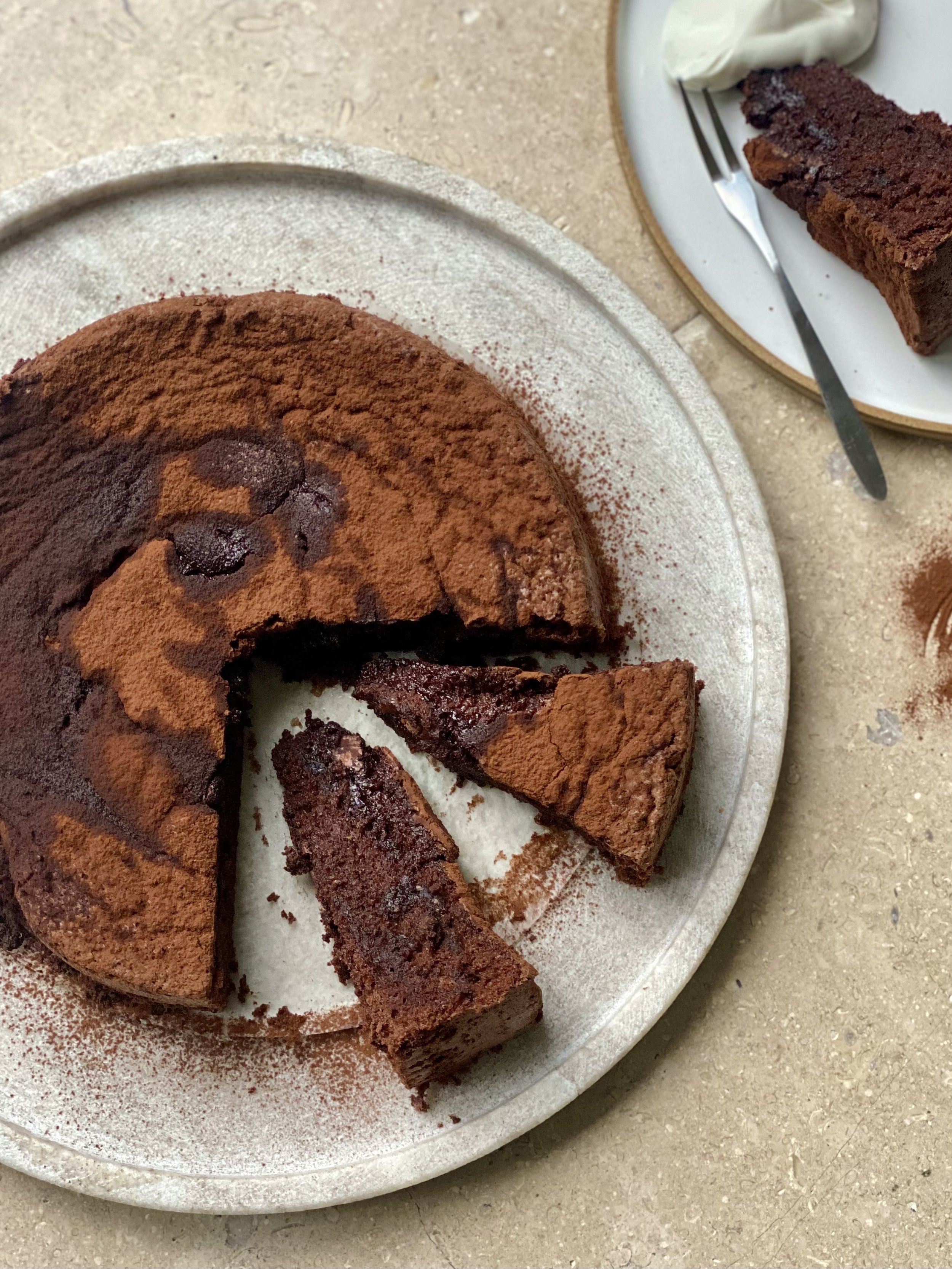 Chocolate cake with a slice cut out, on a white plate with a fork and a dollop of cream