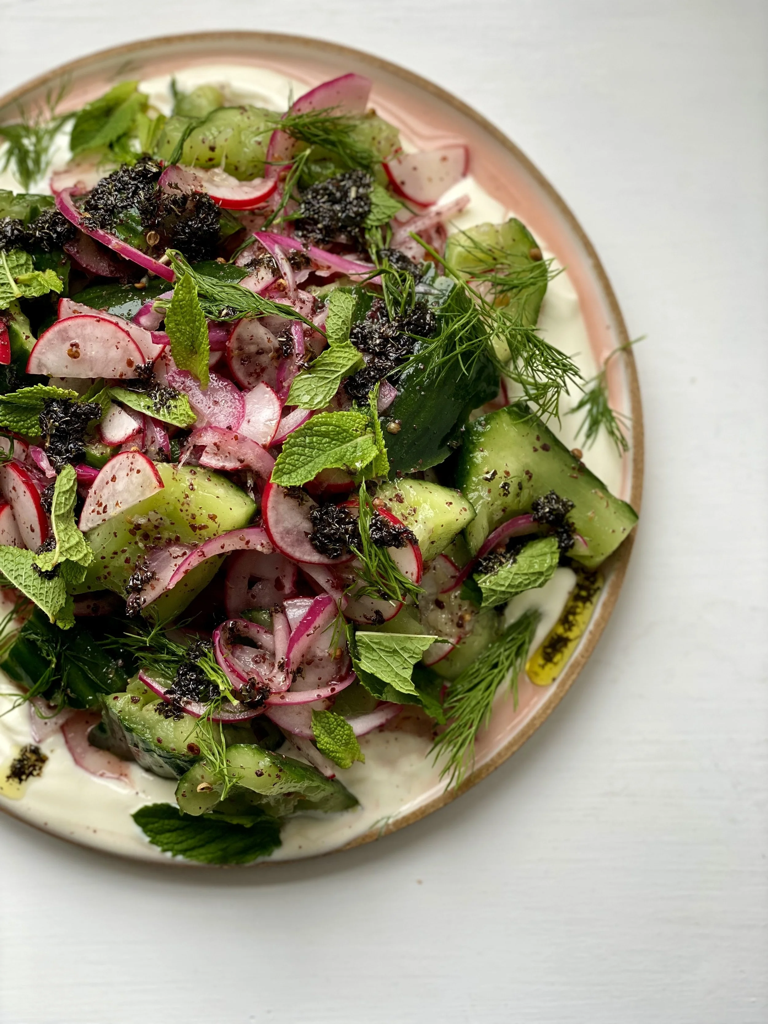 Fresh vegetable salad with radishes, cucumbers, herbs, and black seasoning on a peach-colored plate