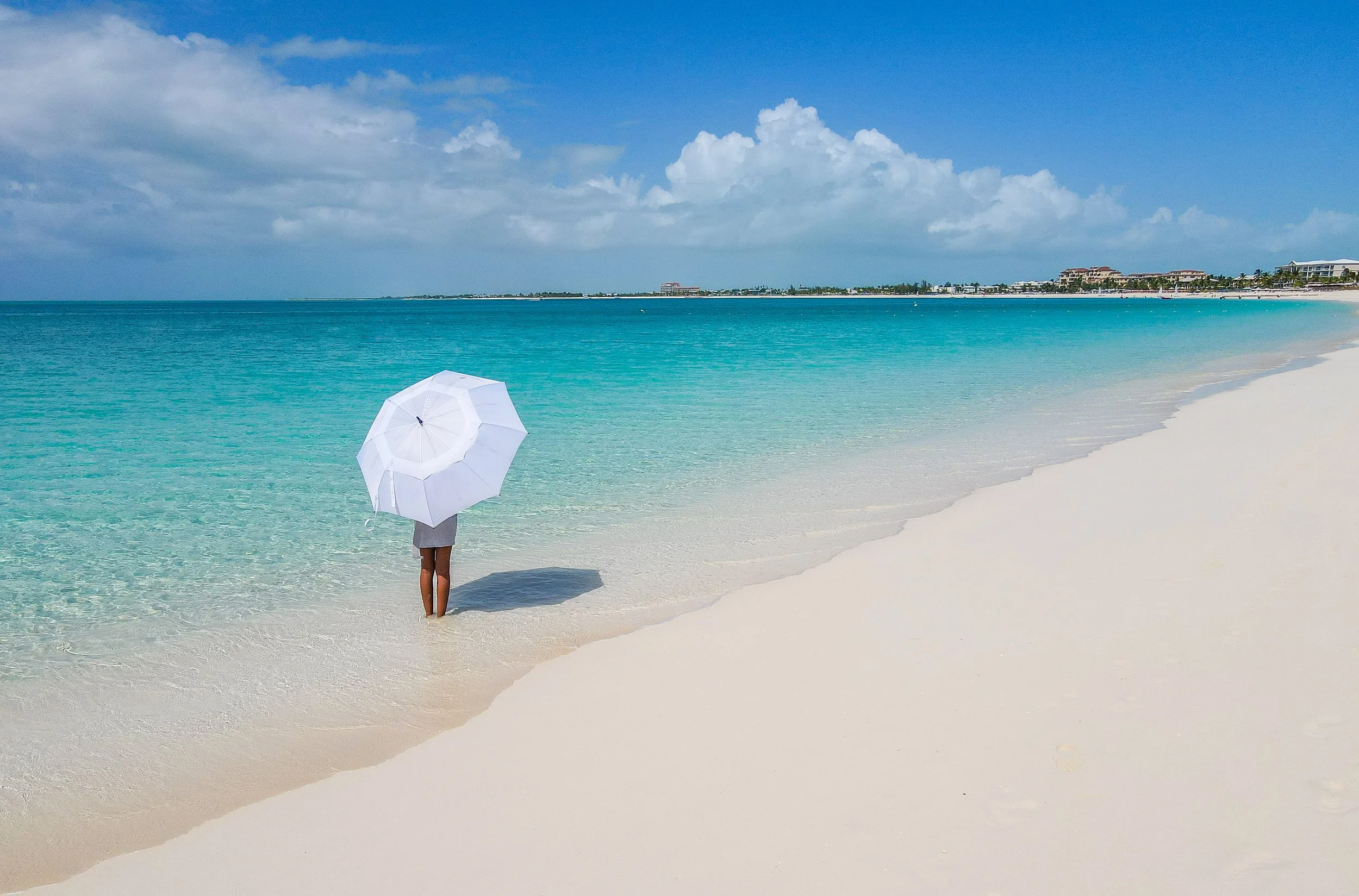 person with parasol on a stretch of white sand and turquoise sea