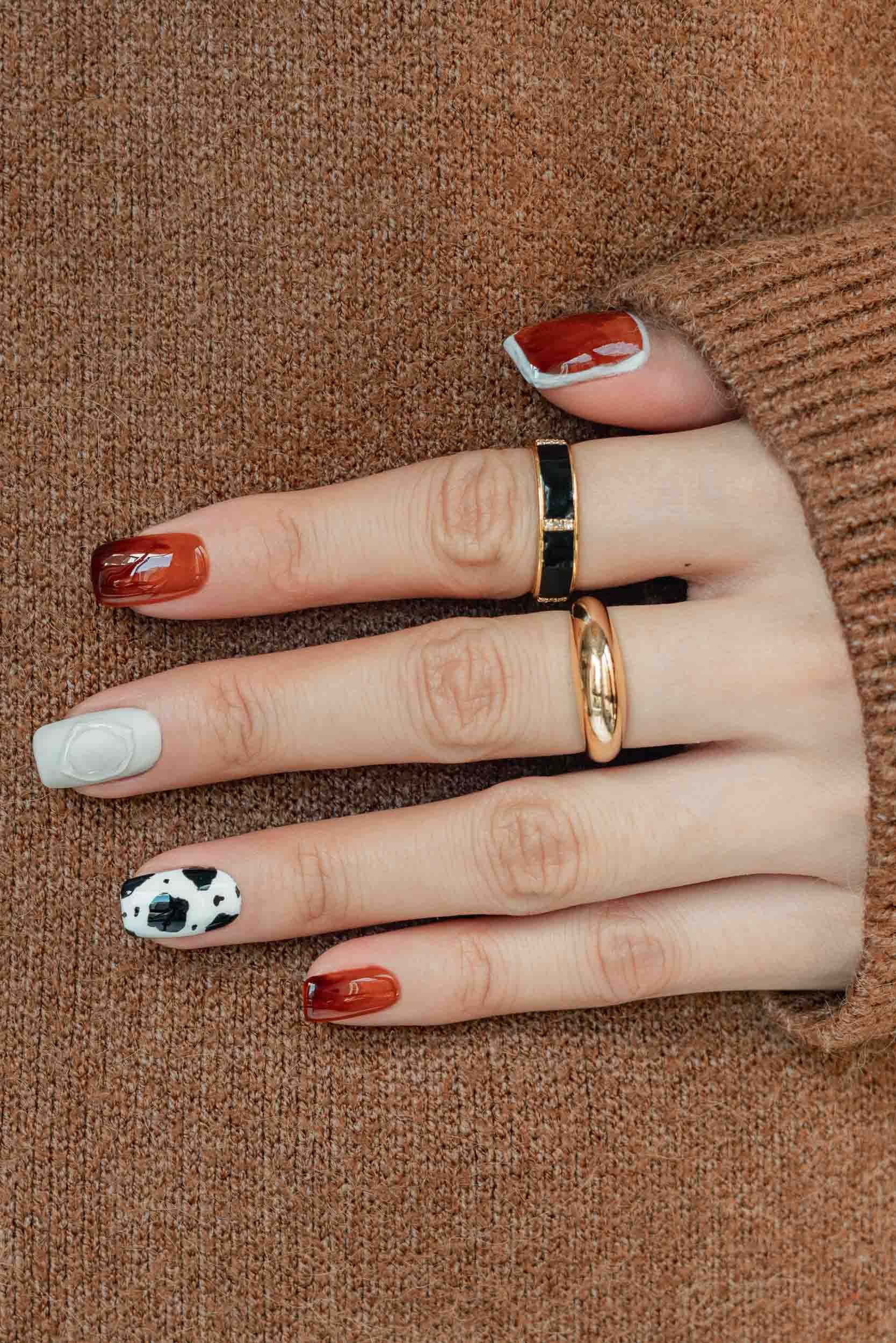 A Becoming Carmen autumn manicure featuring a mixed animal print nail design with tortoiseshell patterns and monochrome cow spots.