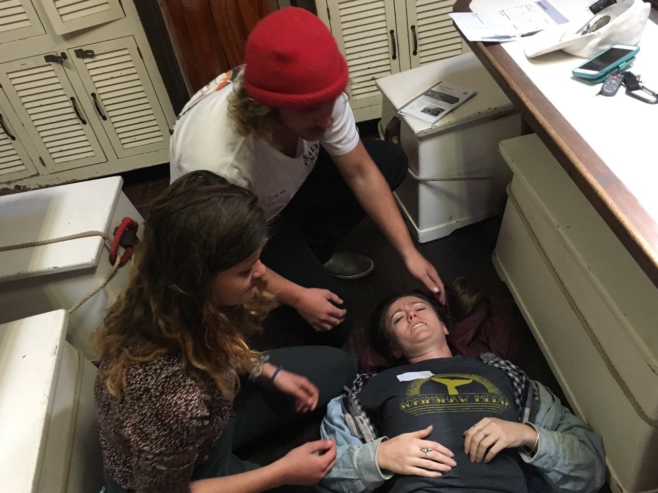   Two participants examining a fellow trainee as she models signs and symptoms of an emergent patient.  