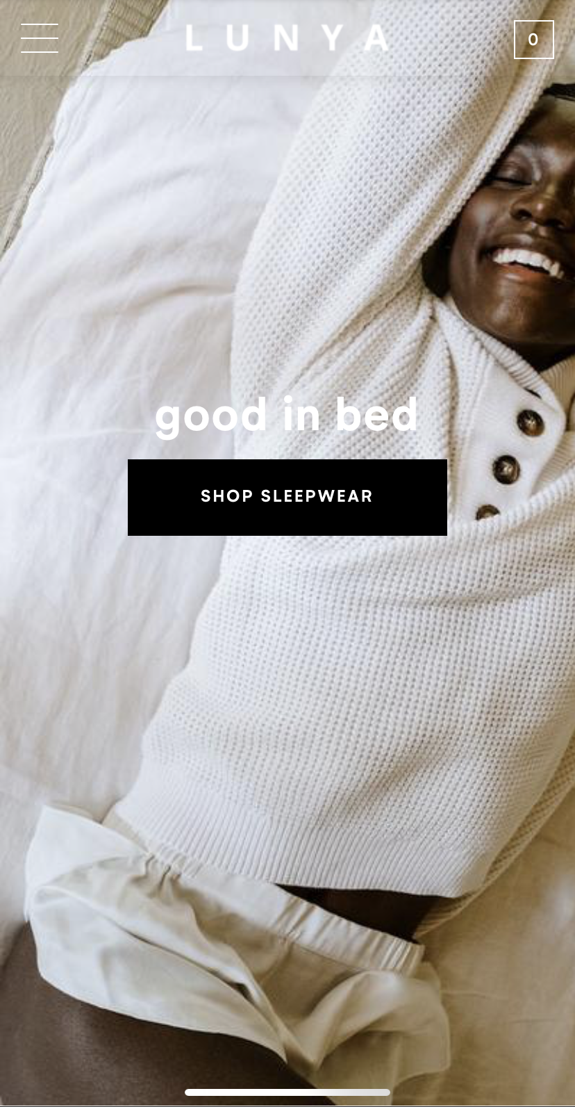 Smiling person lying in bed, cozy white sleepwear, white bedsheets, and blanket, promoting sleepwear for restful sleep.