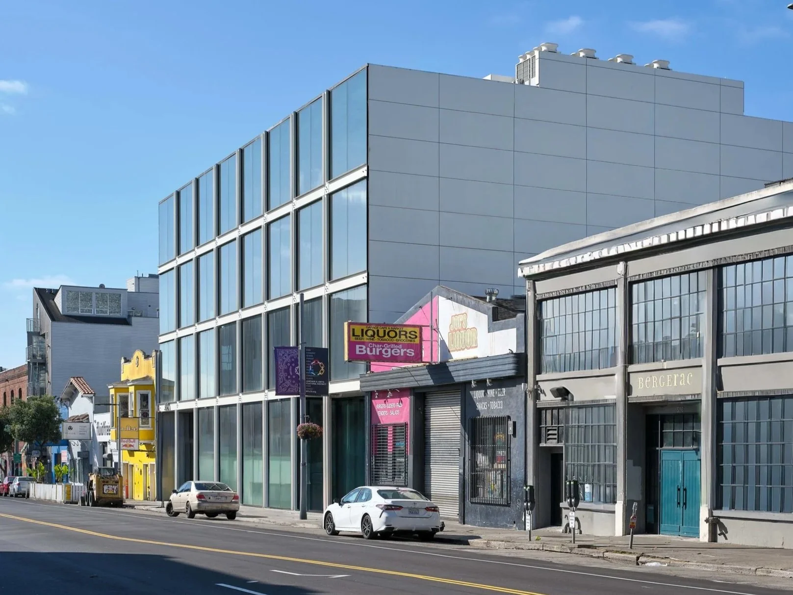 City street with modern glass building, small shops, and parked cars