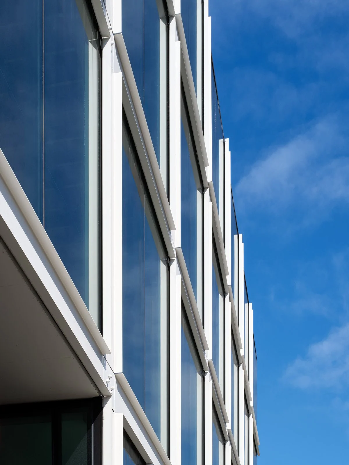 Close-up of a modern glass building with white structural accents against a clear blue sky.