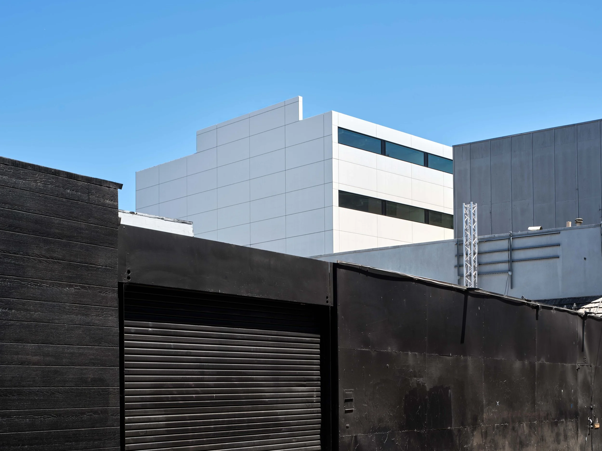 Modern white and gray buildings with a black building in foreground and clear blue sky.