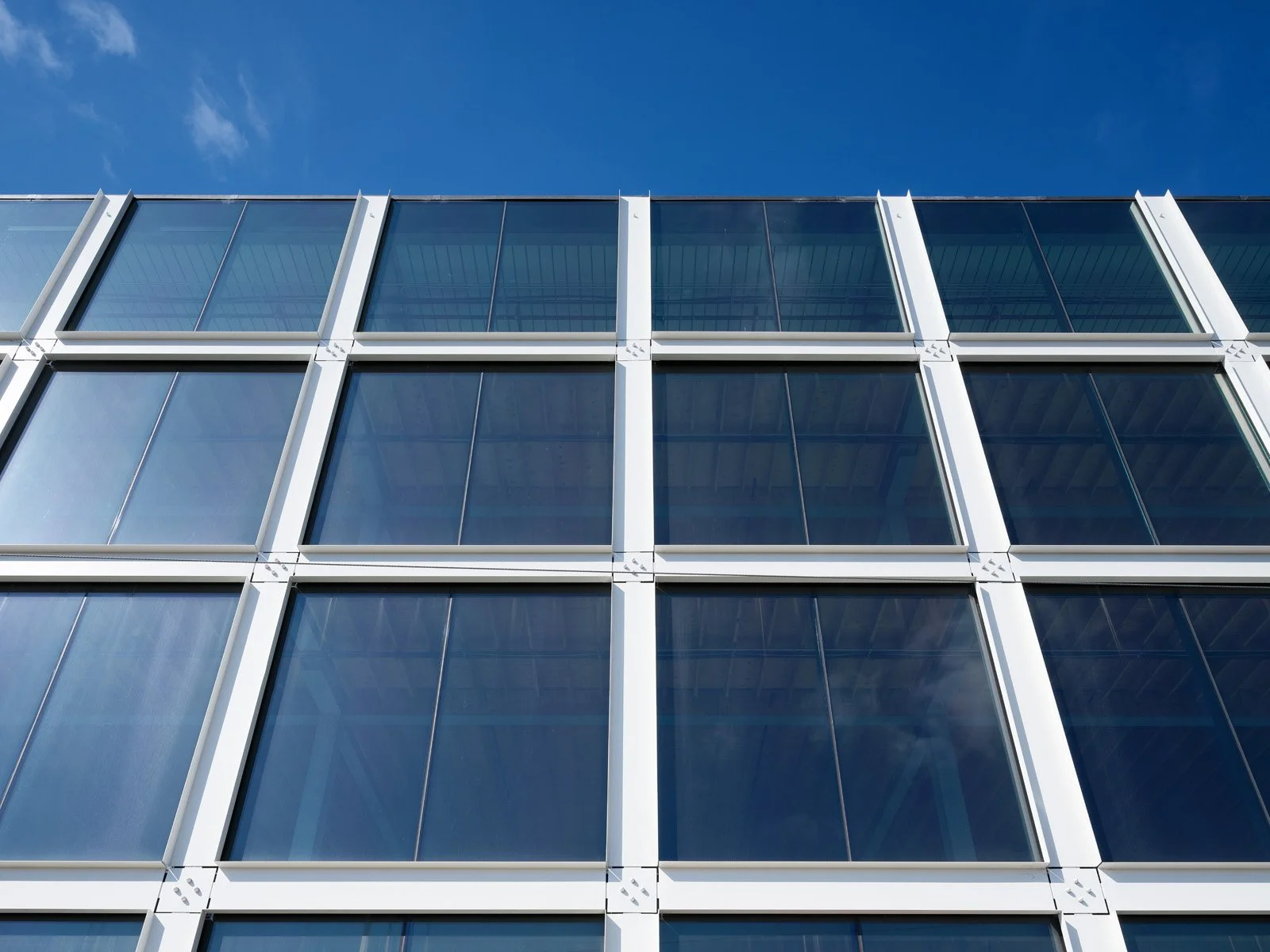 Close-up of a modern glass building facade with multiple windows reflecting the blue sky.