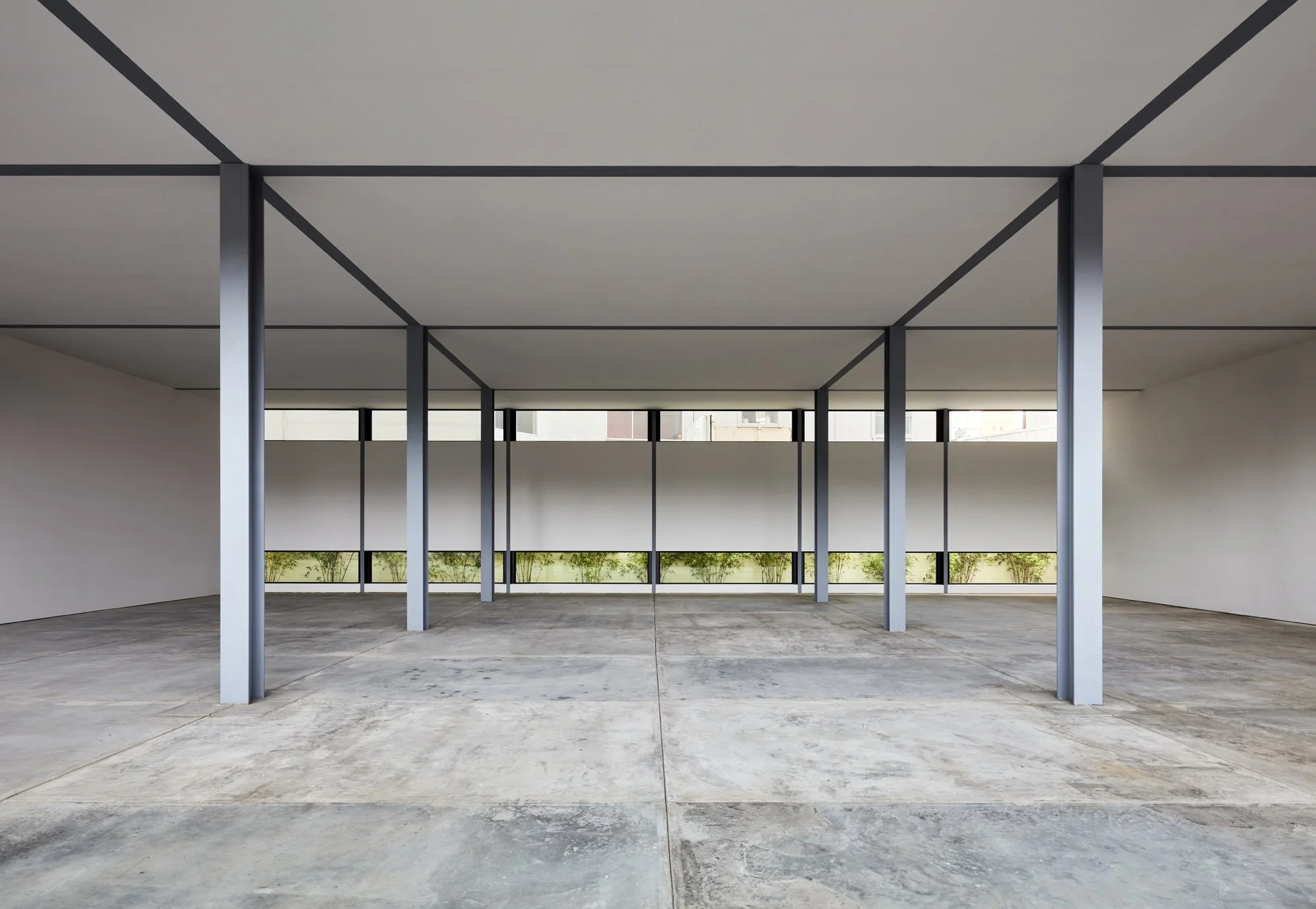Empty modern parking garage with concrete floor, white walls, and metal support columns, large windows at the back letting in natural light.