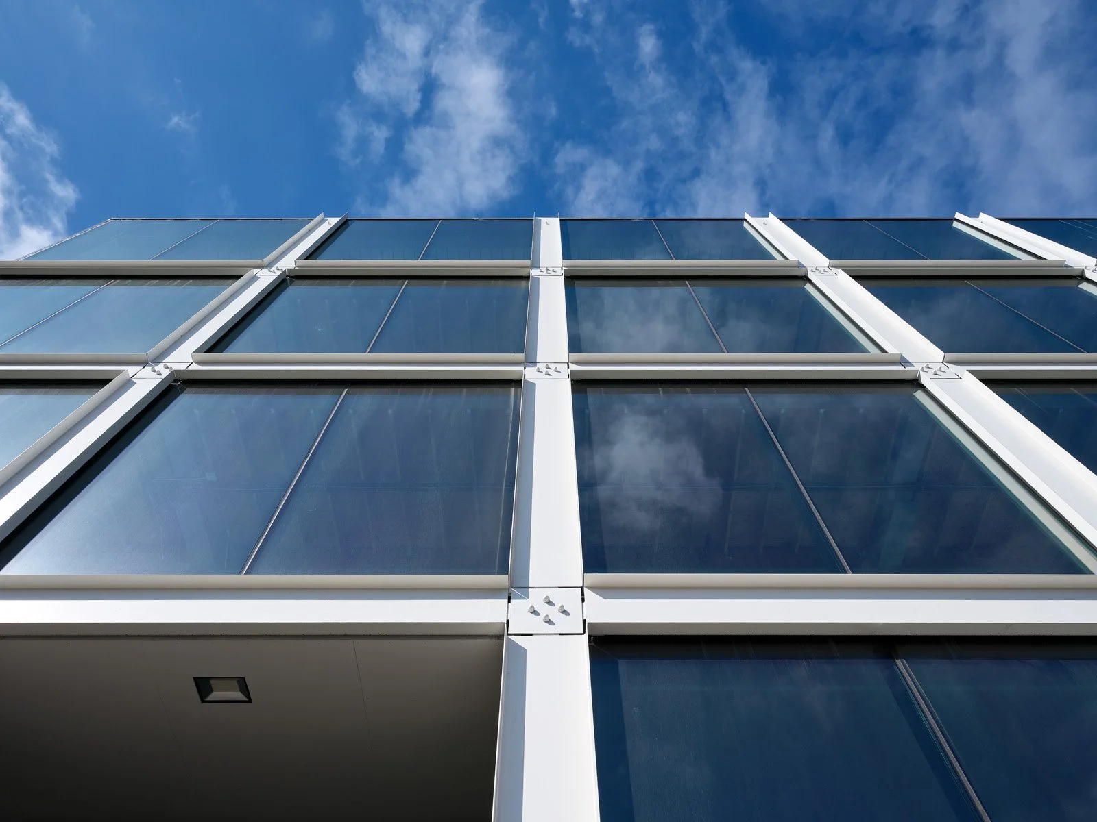 Low-angle view of a modern glass building against a blue sky with clouds.