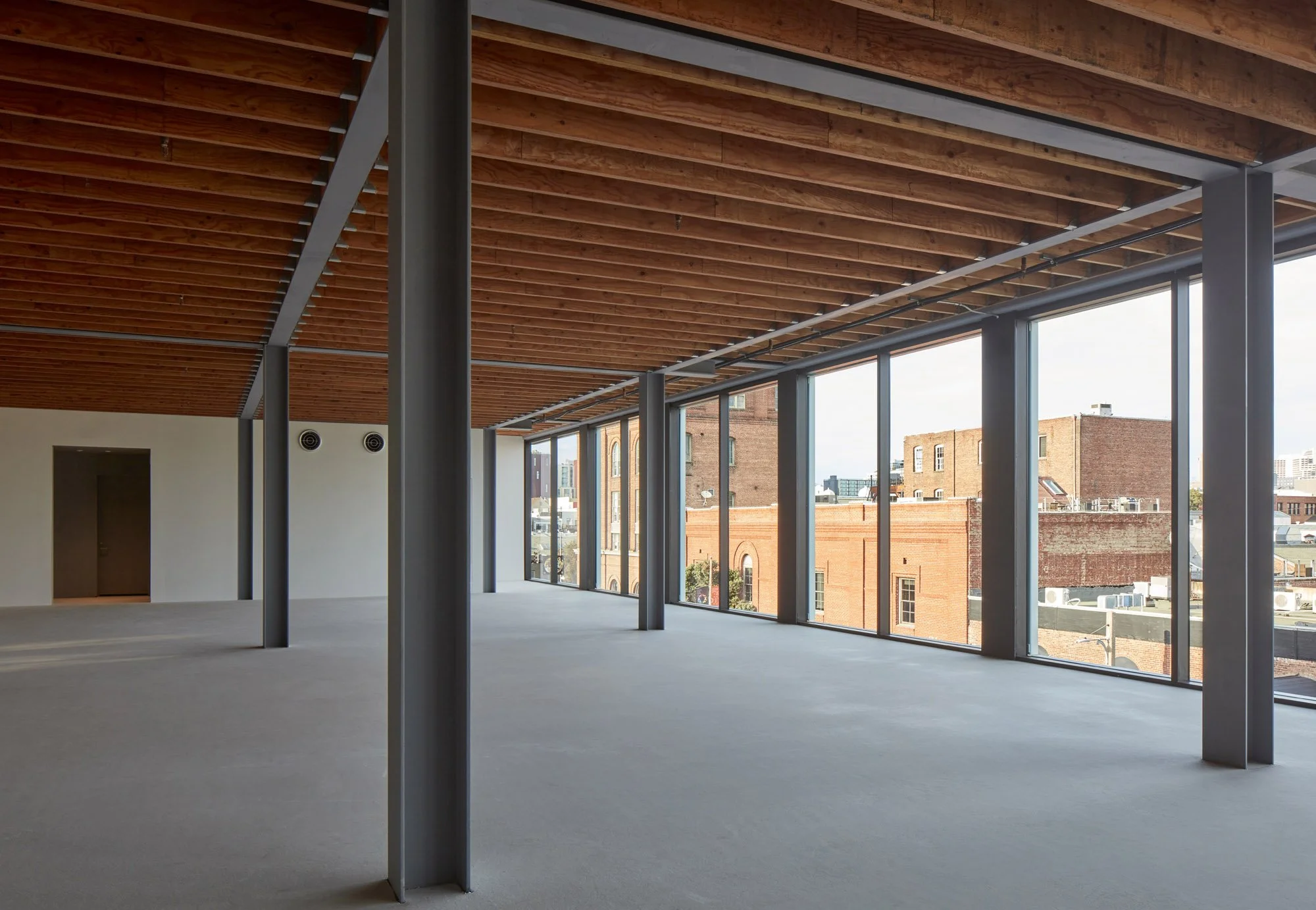 Empty modern office with large floor-to-ceiling windows, wooden ceiling, and steel support columns.