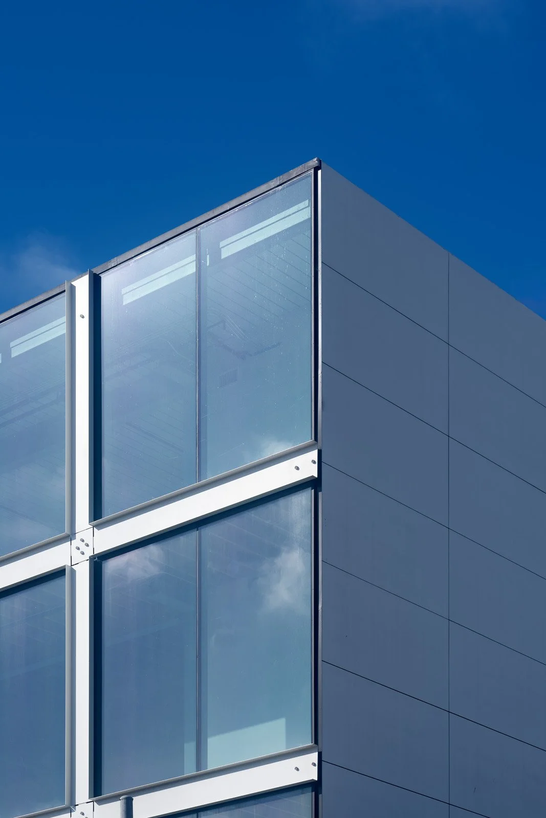 Close-up of modern glass-office building corner with reflective windows against a clear blue sky.