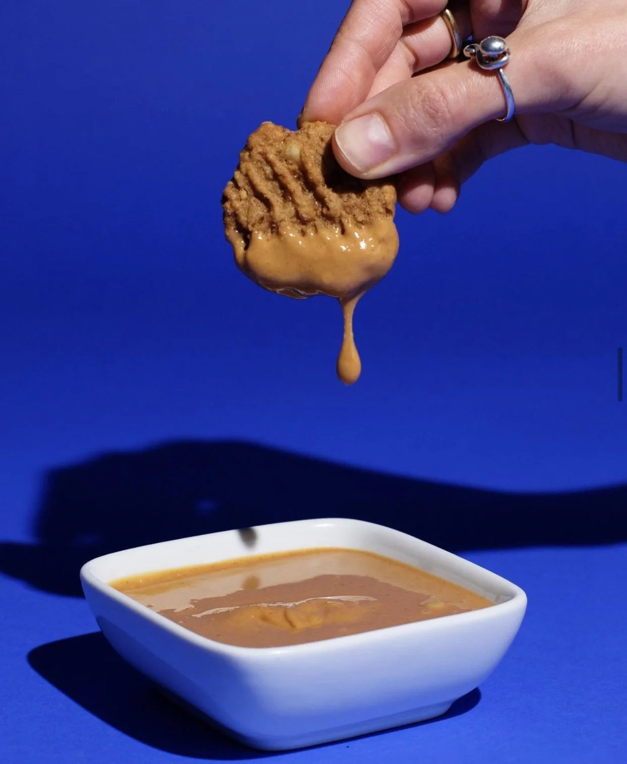 Hand dipping a fried chicken drumstick into a bowl of gravy with a blue background.