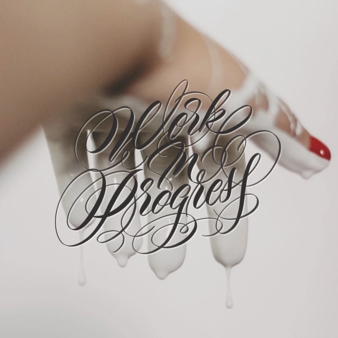 A white dog with red painted nails and a small tongue sticking out, with the words 'Work in Progress' in elegant cursive overlayed.