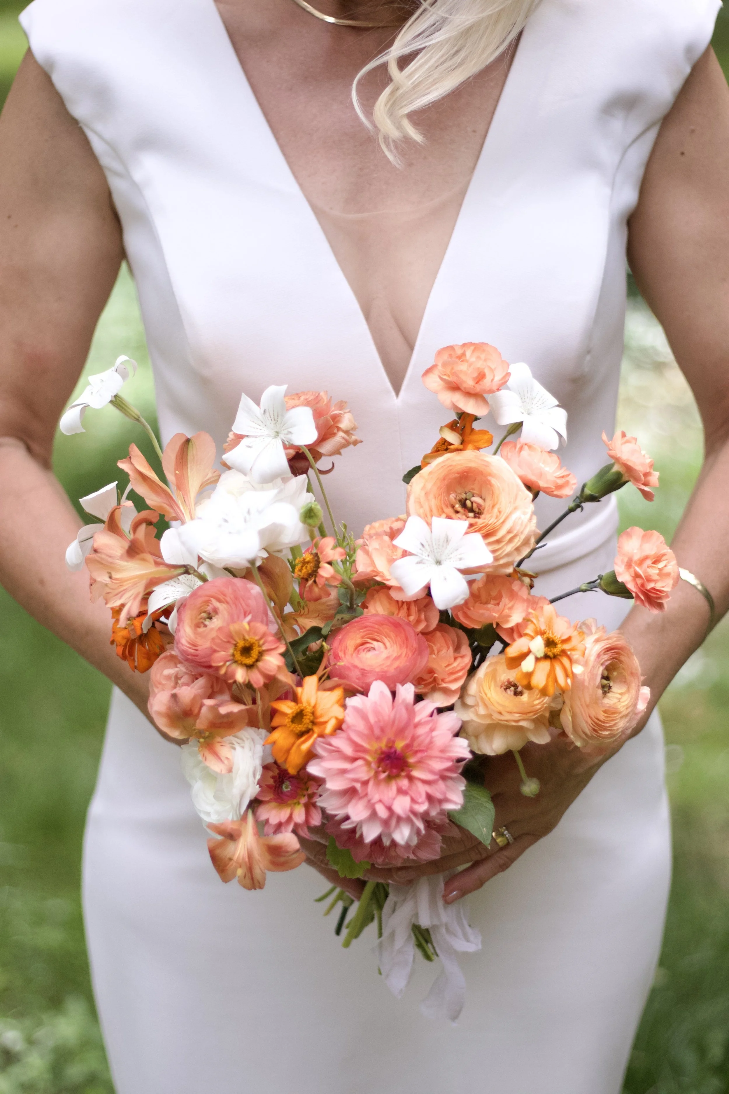 A woman wearing a white dress holding a bouquet of pink, orange, and white flowers.
