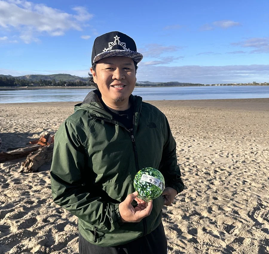 man holding a glass float on the beach, smiling