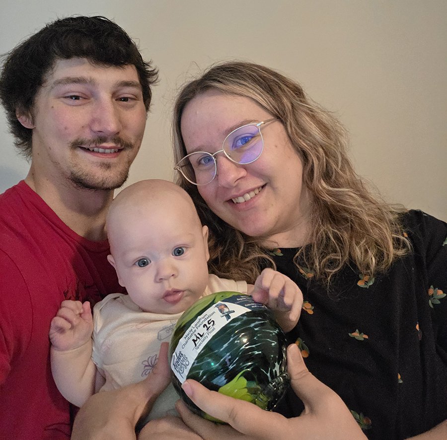 a young family of 3, baby in arms, holding their glass float