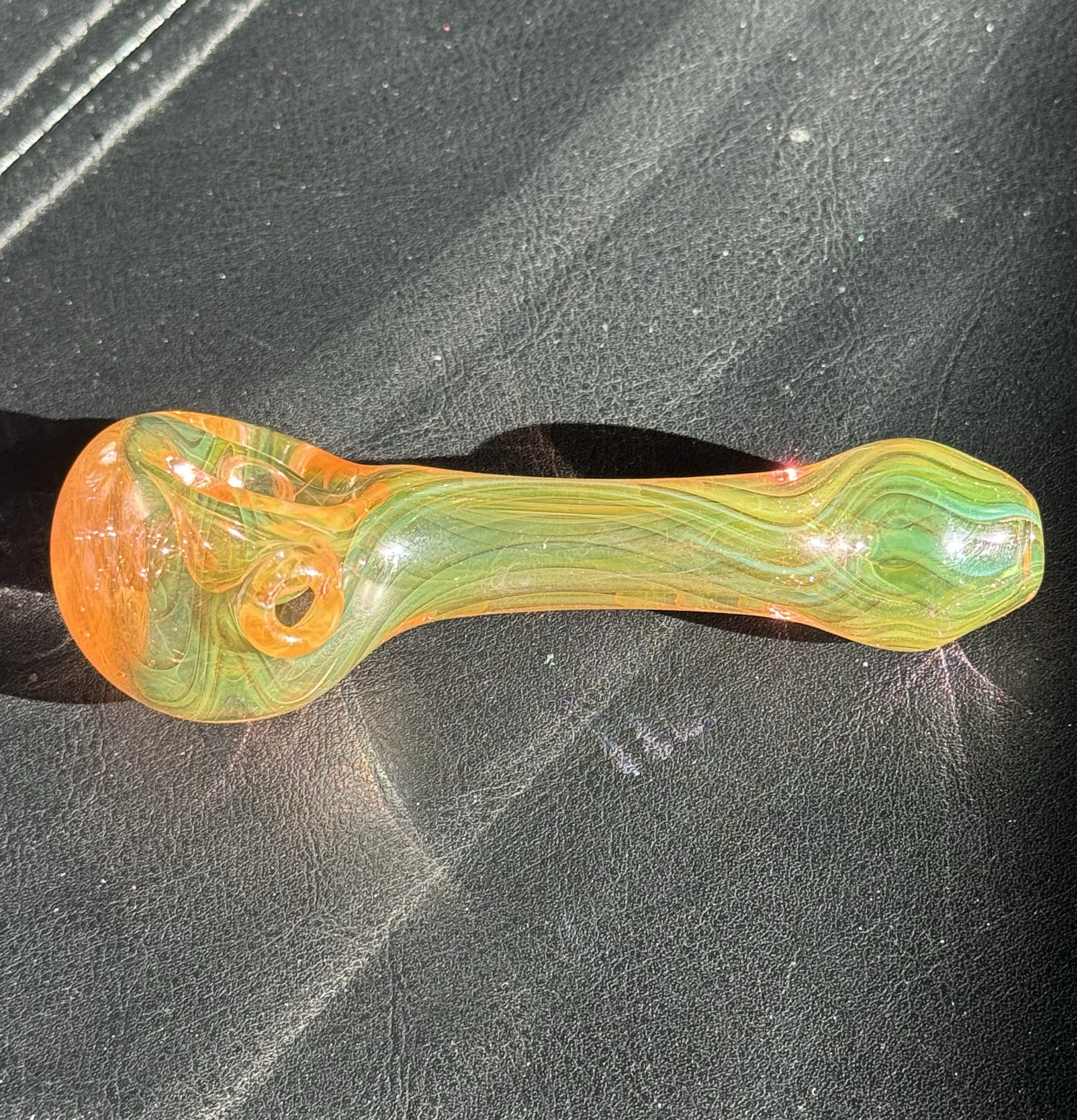 Colorful glass smoking pipe on a black textured surface.