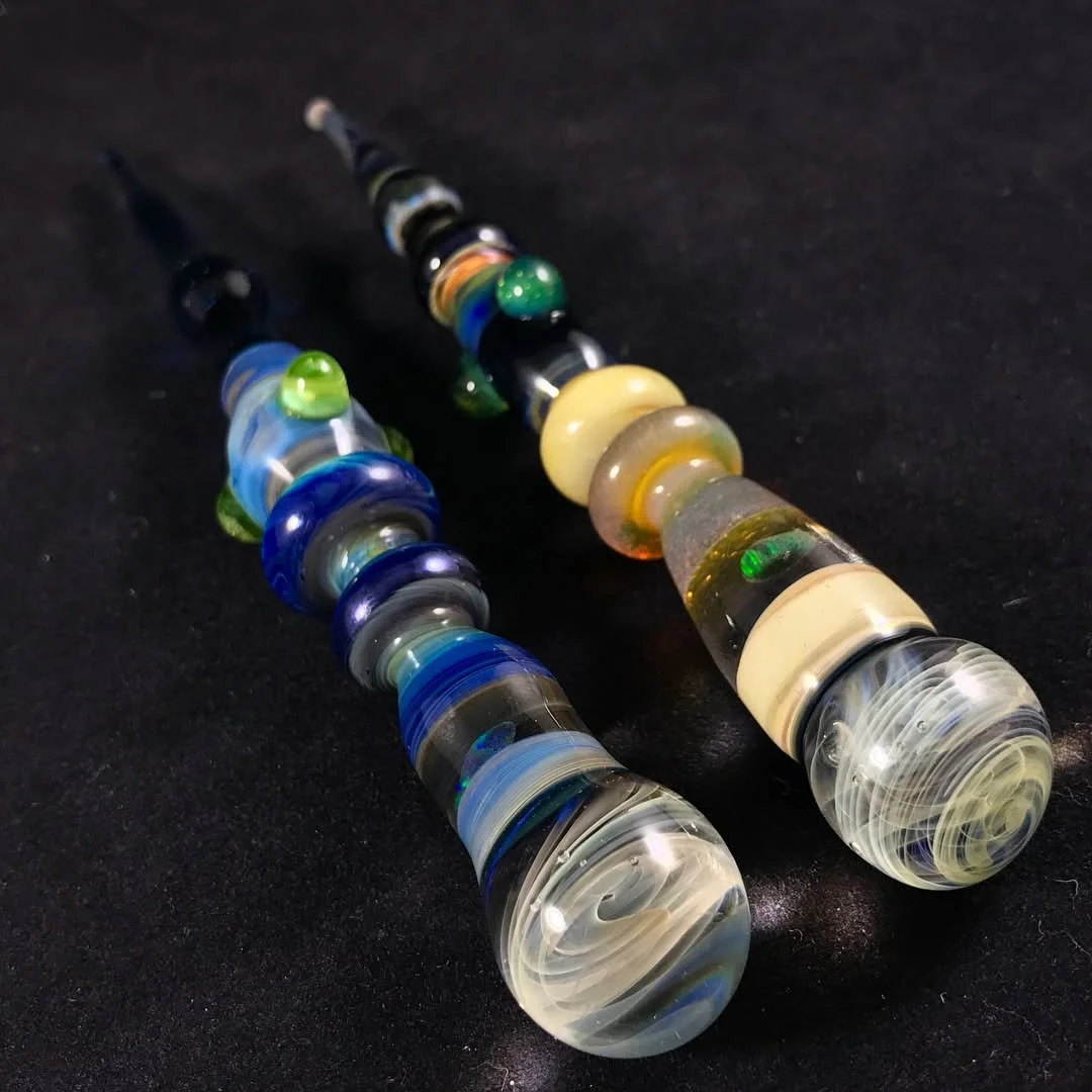 Two glass smoking pipes with colorful swirls on a black surface.