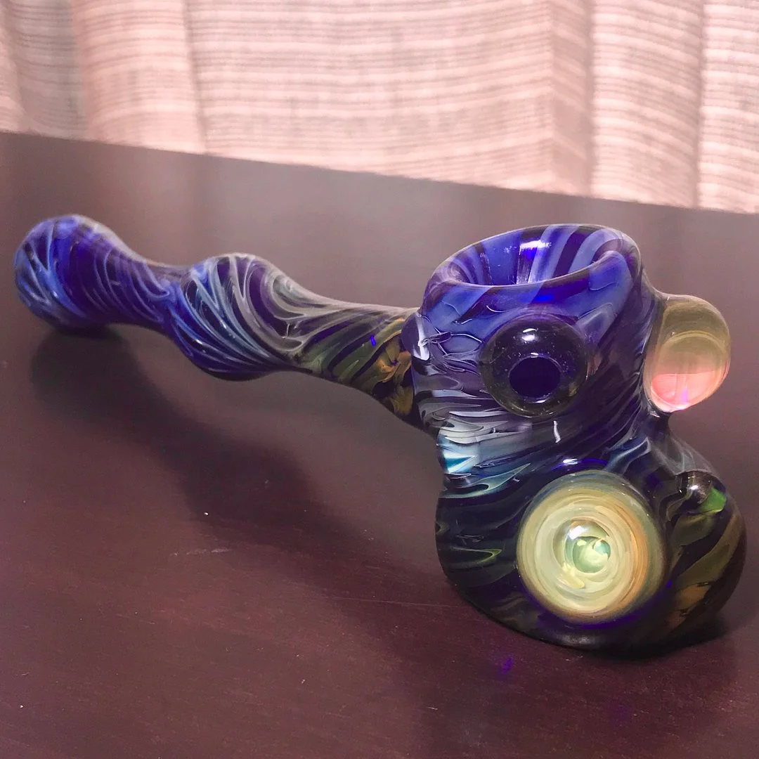 Colorful glass smoking pipe with swirls of purple, yellow, and pink, resting on a dark surface.