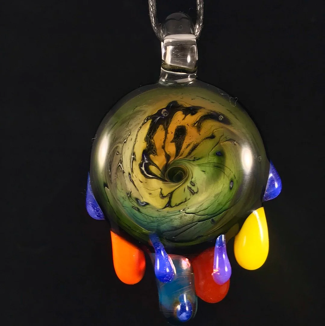 Colorful glass pendant with a swirling pattern and drips of yellow, red, blue, and purple glass hanging from a loop.