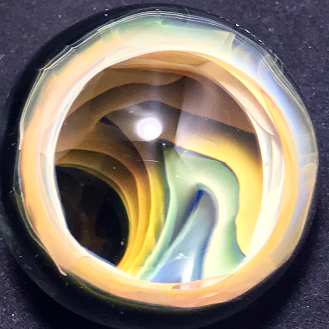 Close-up of a colorful marbled glass paperweight with swirls of yellow, green, black, brown, and blue, on a black background.