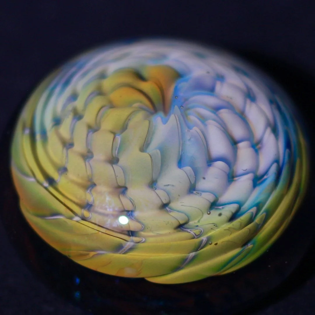Close-up of a colorful glass marble with swirling yellow, blue, and white patterns.