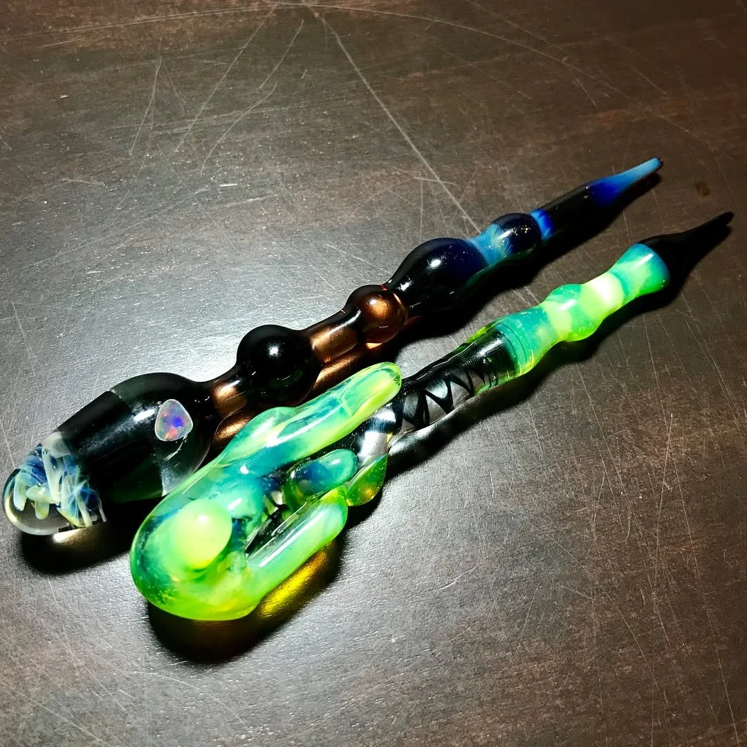 Two colorful glass smoking pipes on a dark surface.