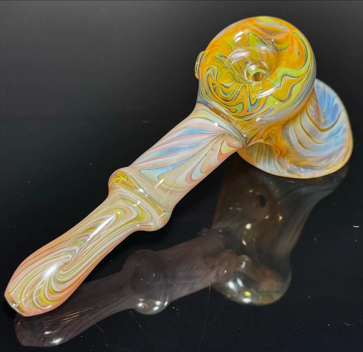 Colorful marble glass pipe with swirls of yellow, blue, pink, and orange, resting on a reflective black surface.