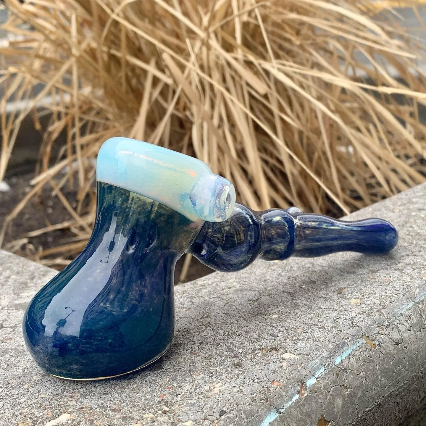 Glass pipe lying on a stone surface with dried grass in the background.