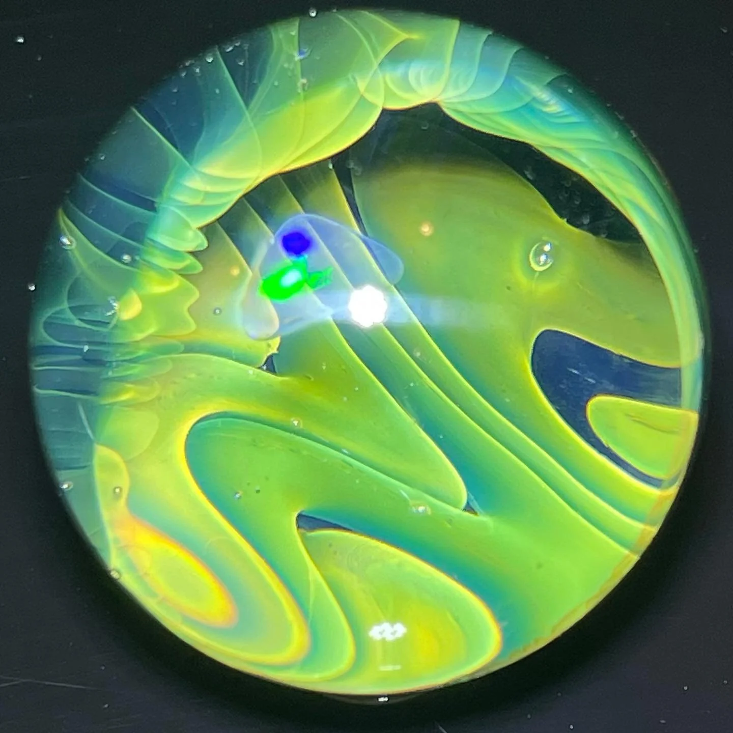 Close-up of a glass marble with swirling yellow and blue colors inside.