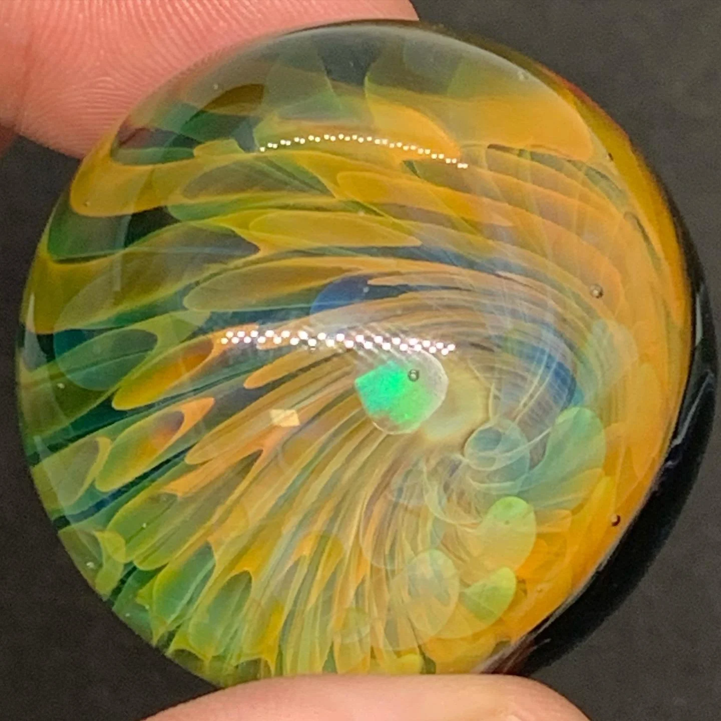 Close-up of a hand holding a multicolored glass paperweight with swirling yellow, green, and blue patterns inside.