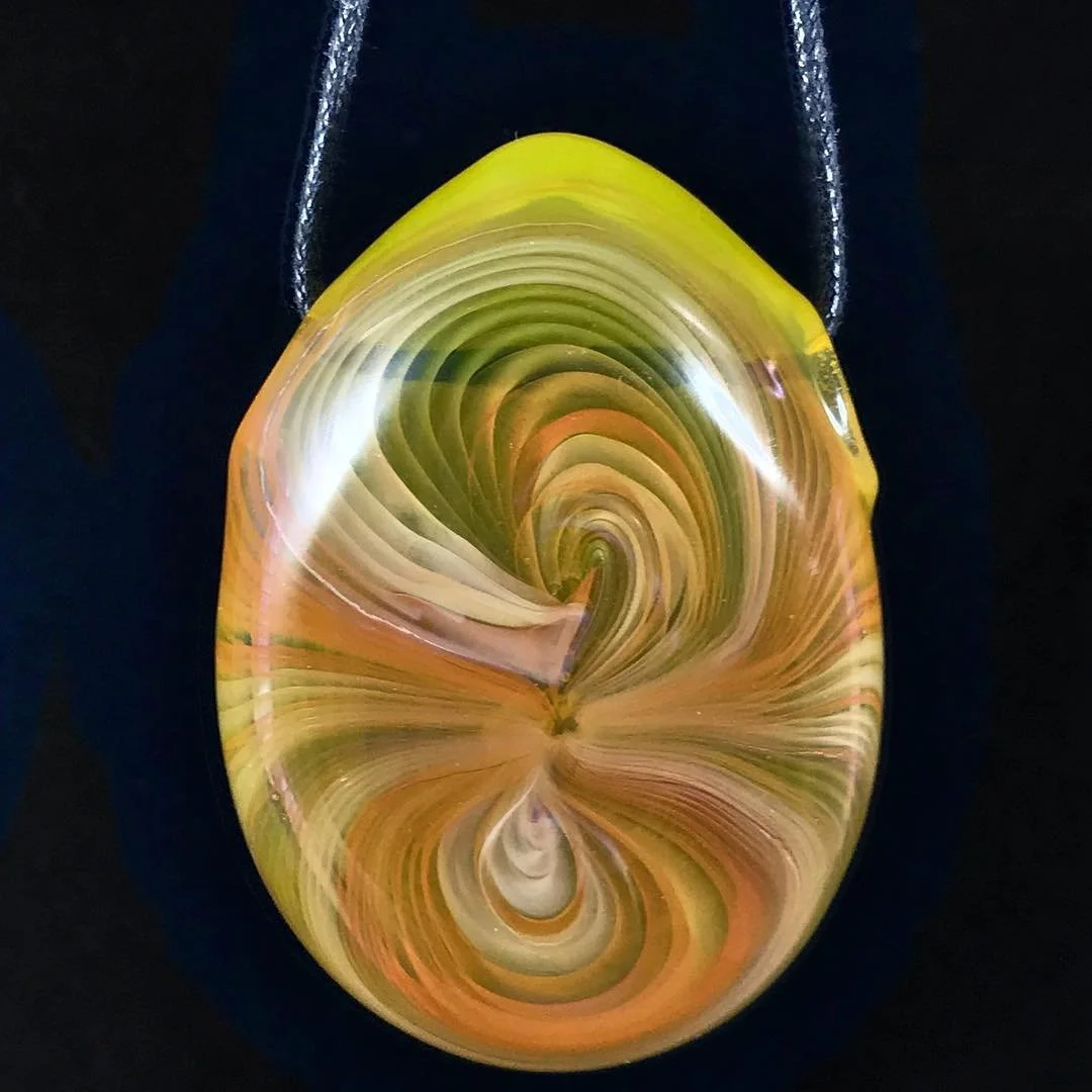 A marbled glass pendant with swirls of yellow, green, cream, and orange, hanging from a black lanyard.