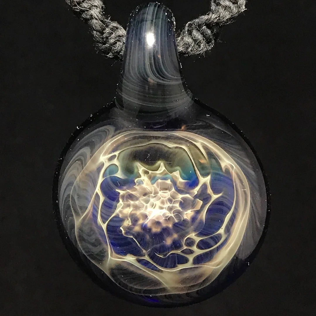 A glass pendant with a swirling, colorful abstract design, hanging from a textured gray cord.