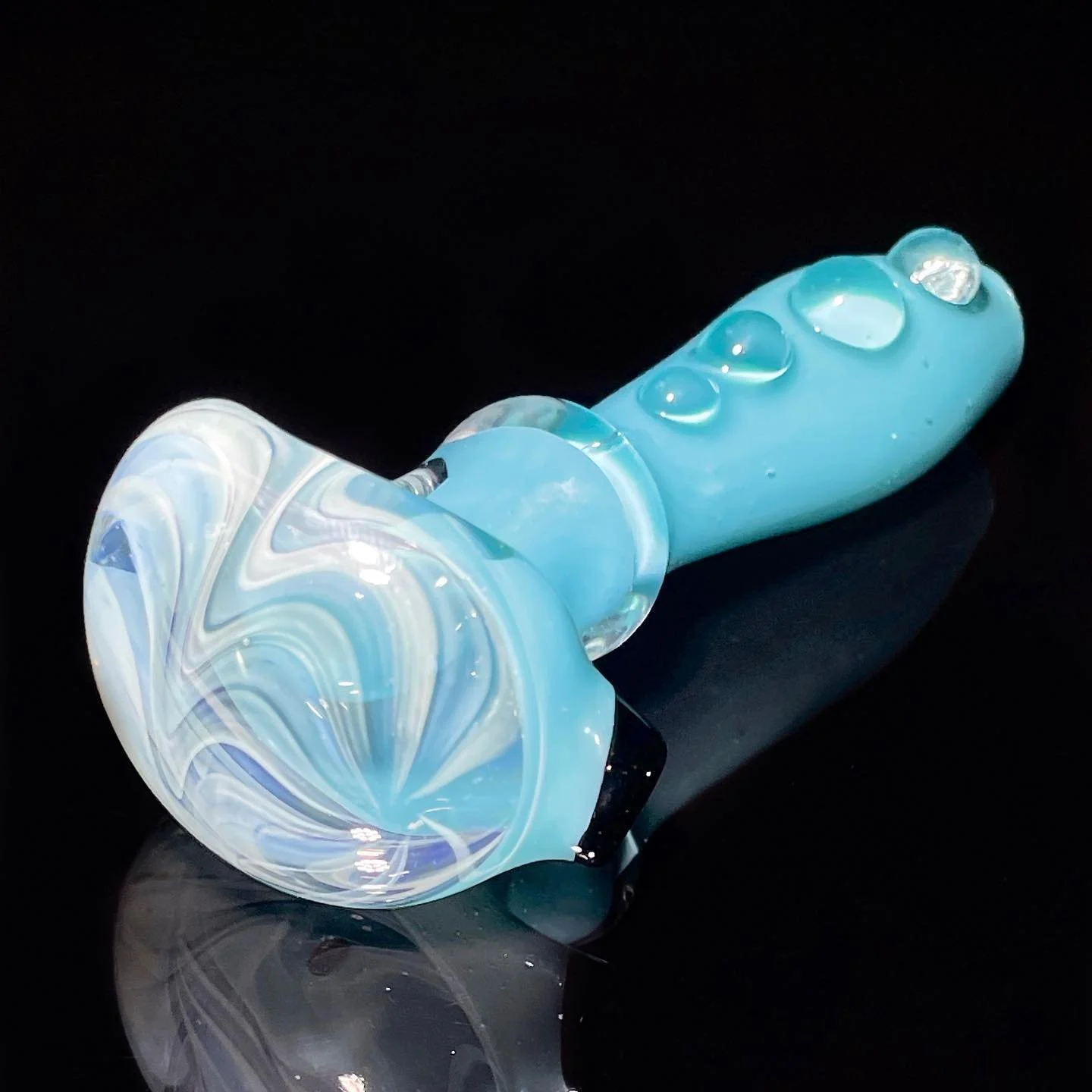 Blue glass pipe with a marble design, resting on a black reflective surface.