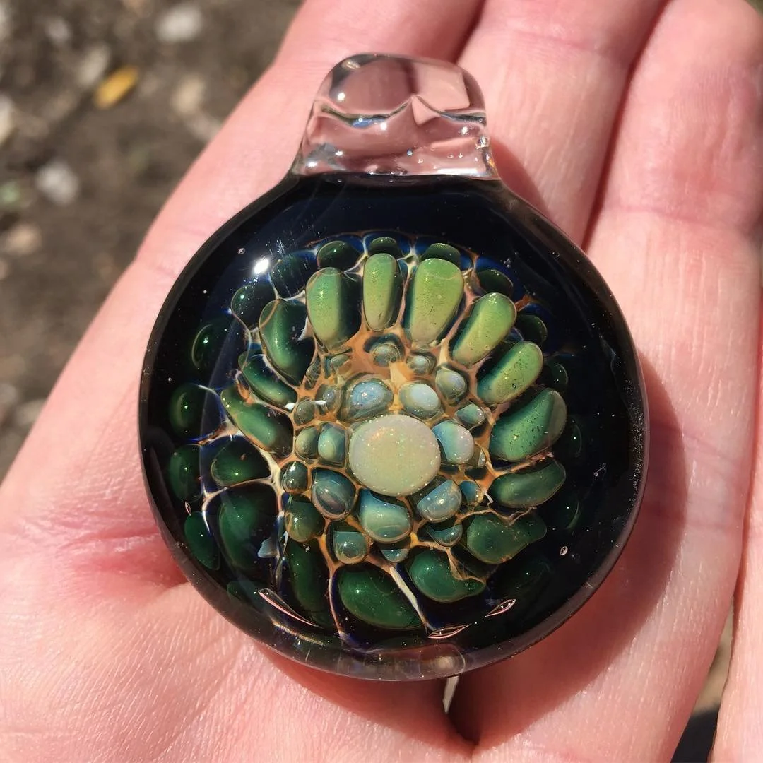 Close-up of a glass pendant with an intricate, colorful floral-like pattern inside, held against a hand.