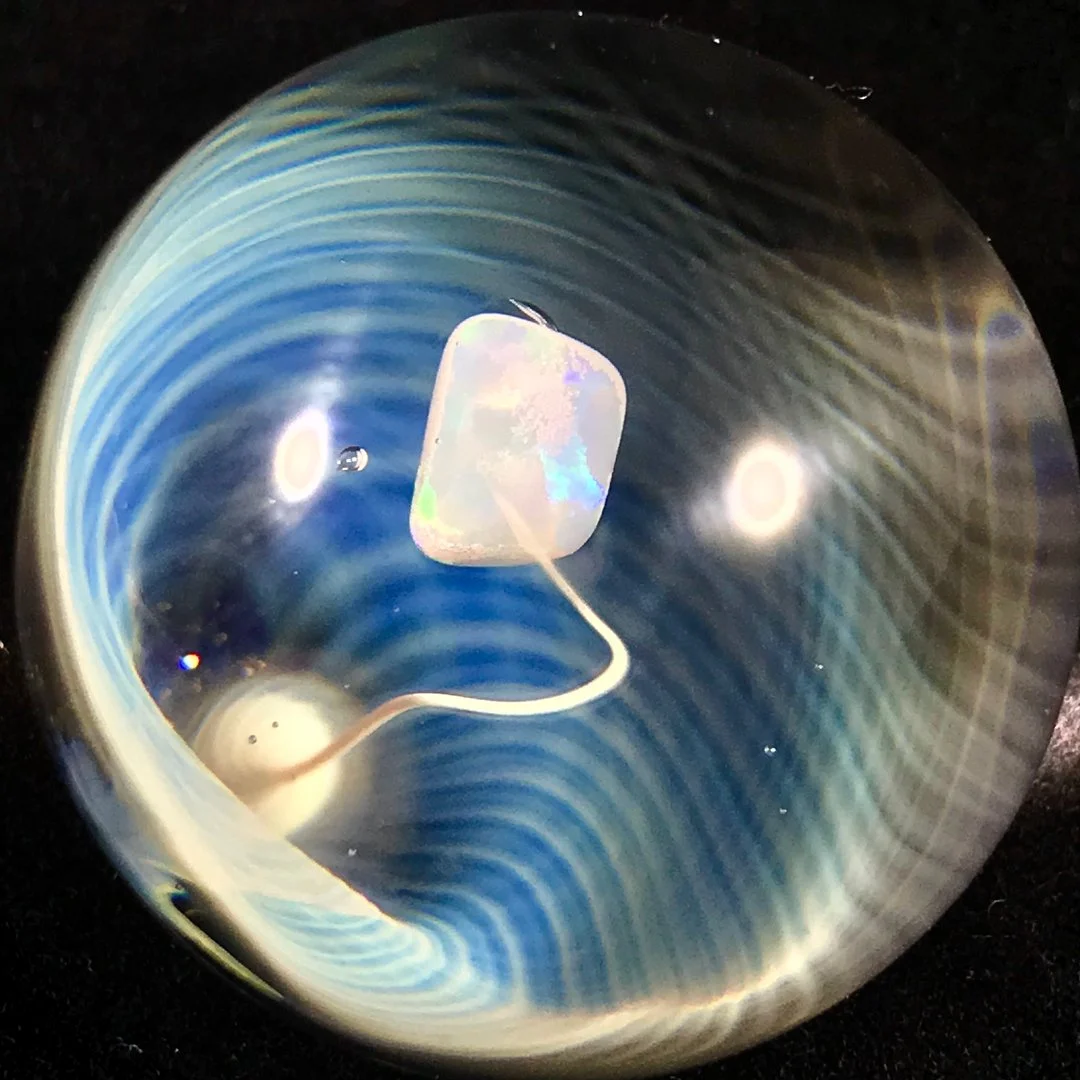Close-up of a small, iridescent object inside a transparent sphere with swirling blue and gold patterns