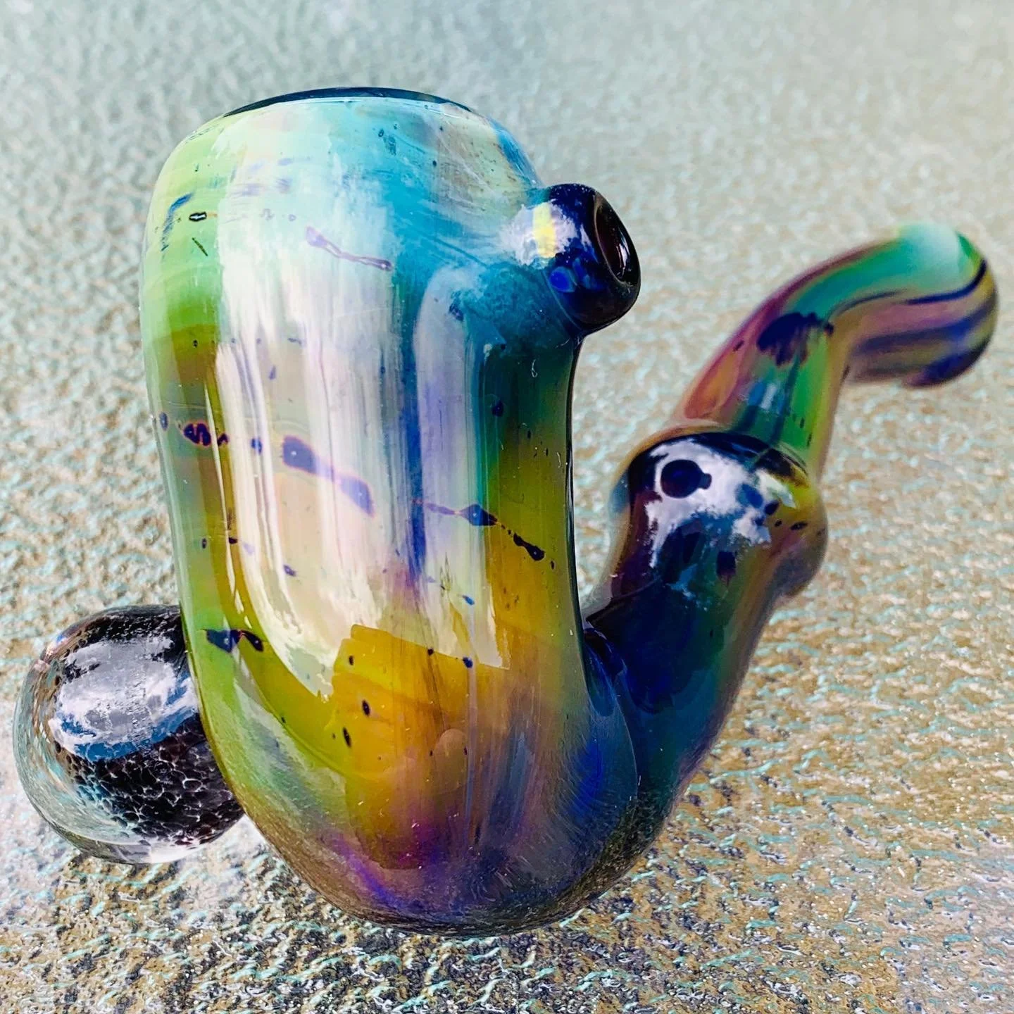 Colorful glass pipe with swirls of blue, green, yellow, and purple on a textured surface.