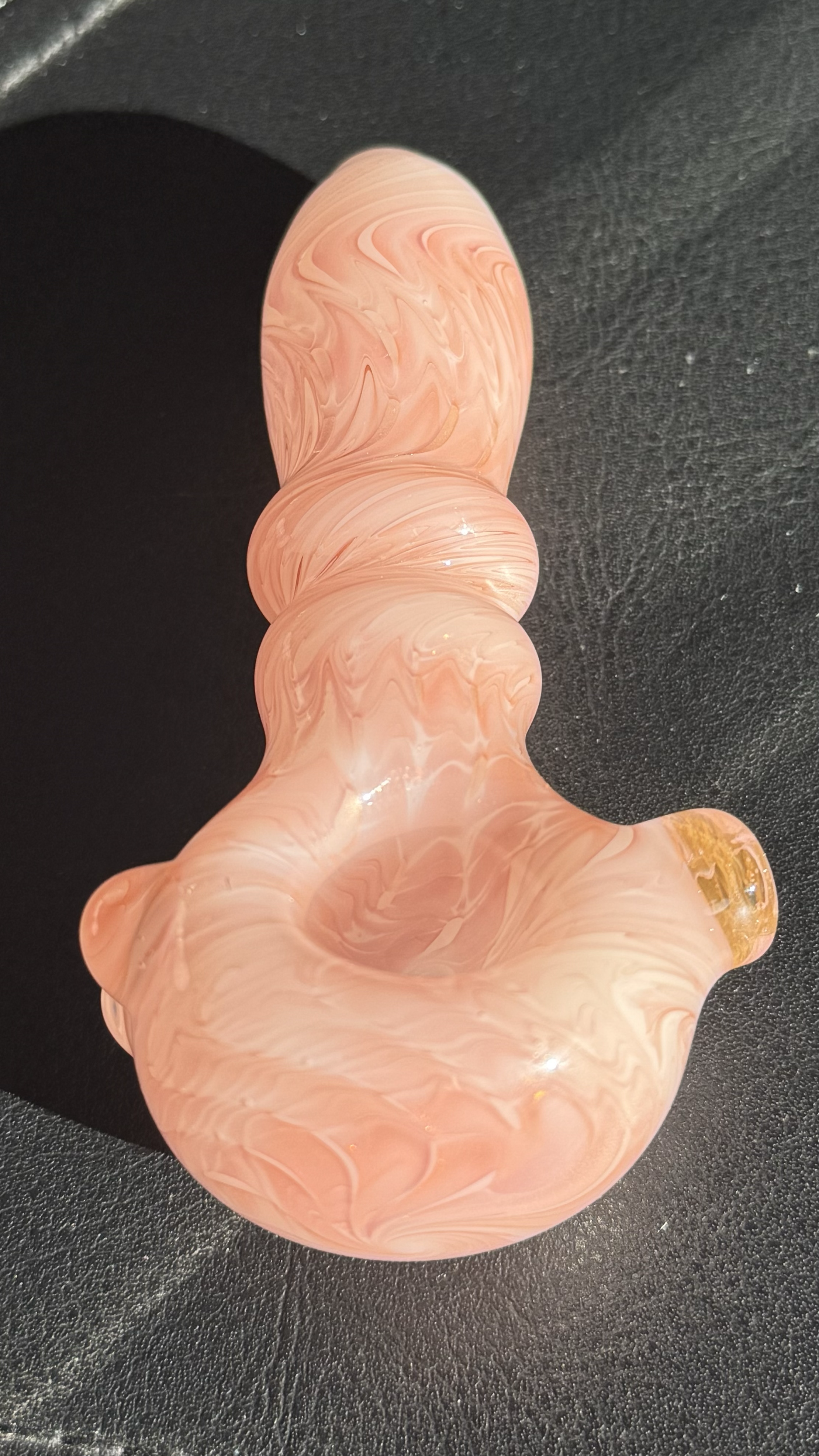 Pink and white marbled glass object with multiple bulbous and curved sections, placed on a black surface.