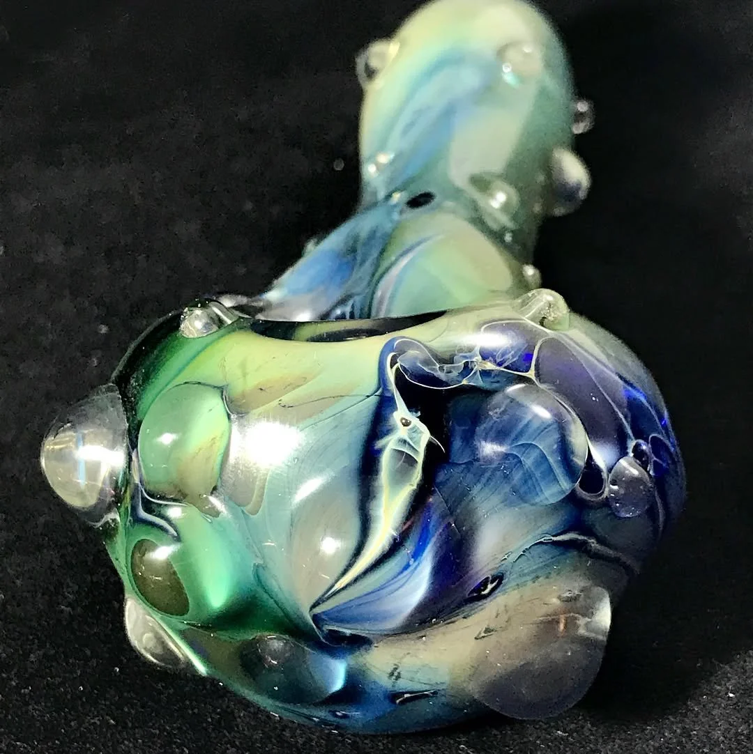 Close-up of a multicolored glass art piece with swirls of green, blue, and yellow, on a black surface.