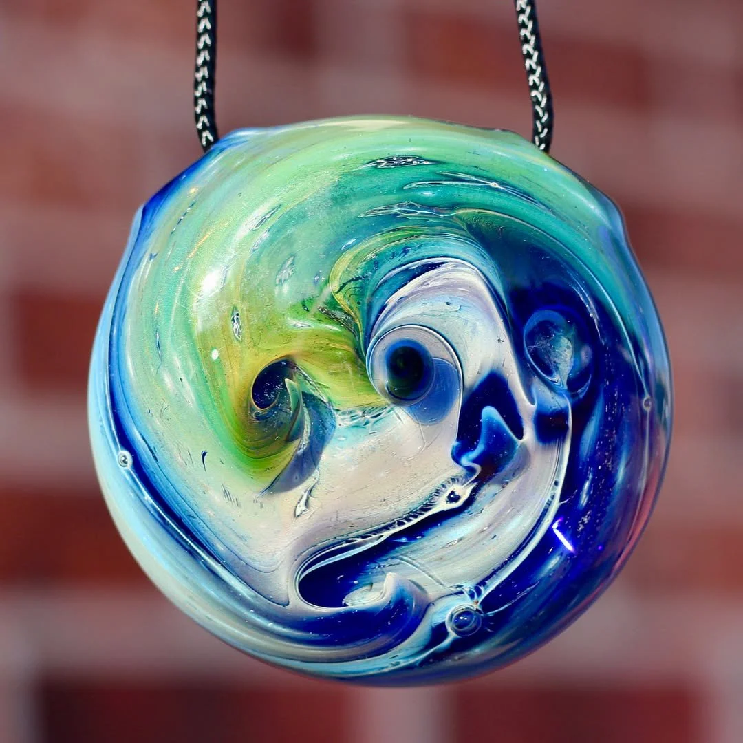 Close-up of a colorful glass orbs pendant with swirling blue, green, and white patterns, hanging from a black and white cord.