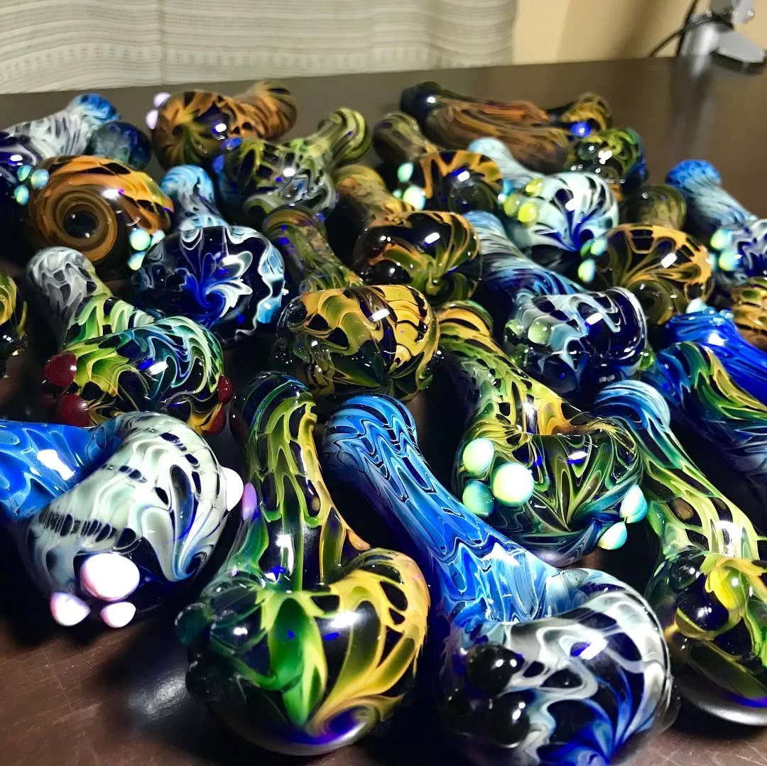 Colorful glass art pipes with swirling patterns, some glowing with LED lights, scattered on a dark surface.