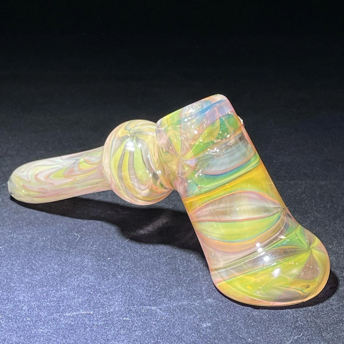 Colorful glass pipe with swirled yellow, pink, green, and blue patterns on a black surface.