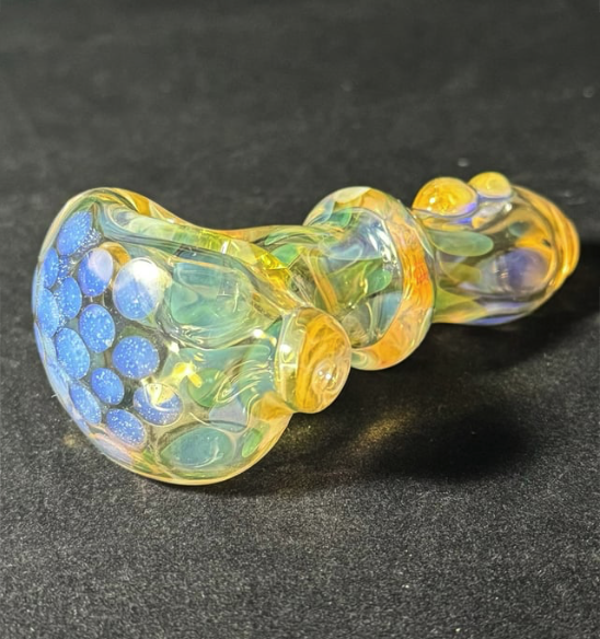 Colorful glass pipe with yellow, blue, and green swirling patterns on a black surface.
