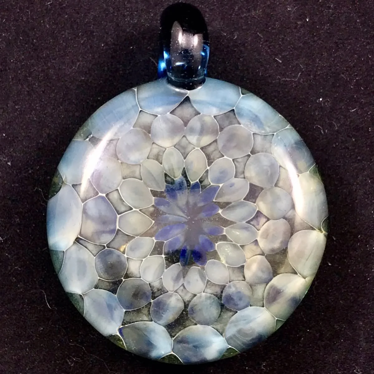 A round glass pendant with a floral mosaic pattern in shades of white, blue, and purple, featuring a black bail at the top for jewelry attachment.