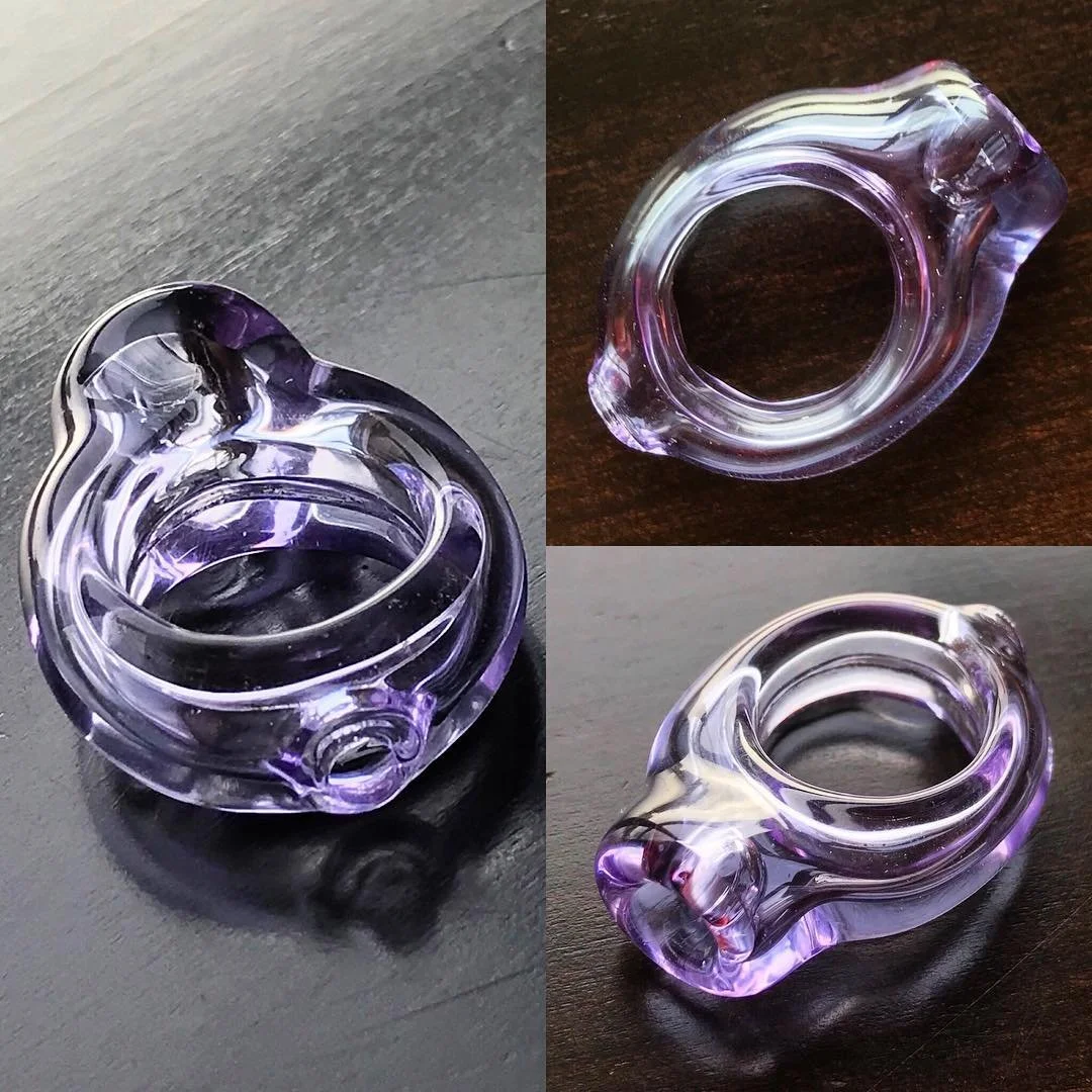 A small glass ring with purple and clear swirls, shown from three angles on dark surfaces.