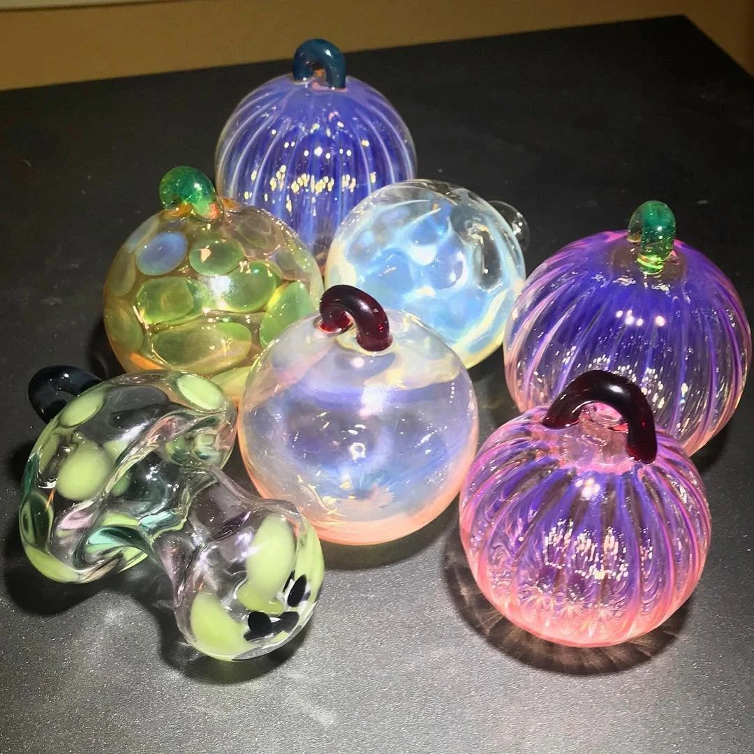 Colorful glass pumpkins with vibrant purple, blue, green, and black details on a black surface.