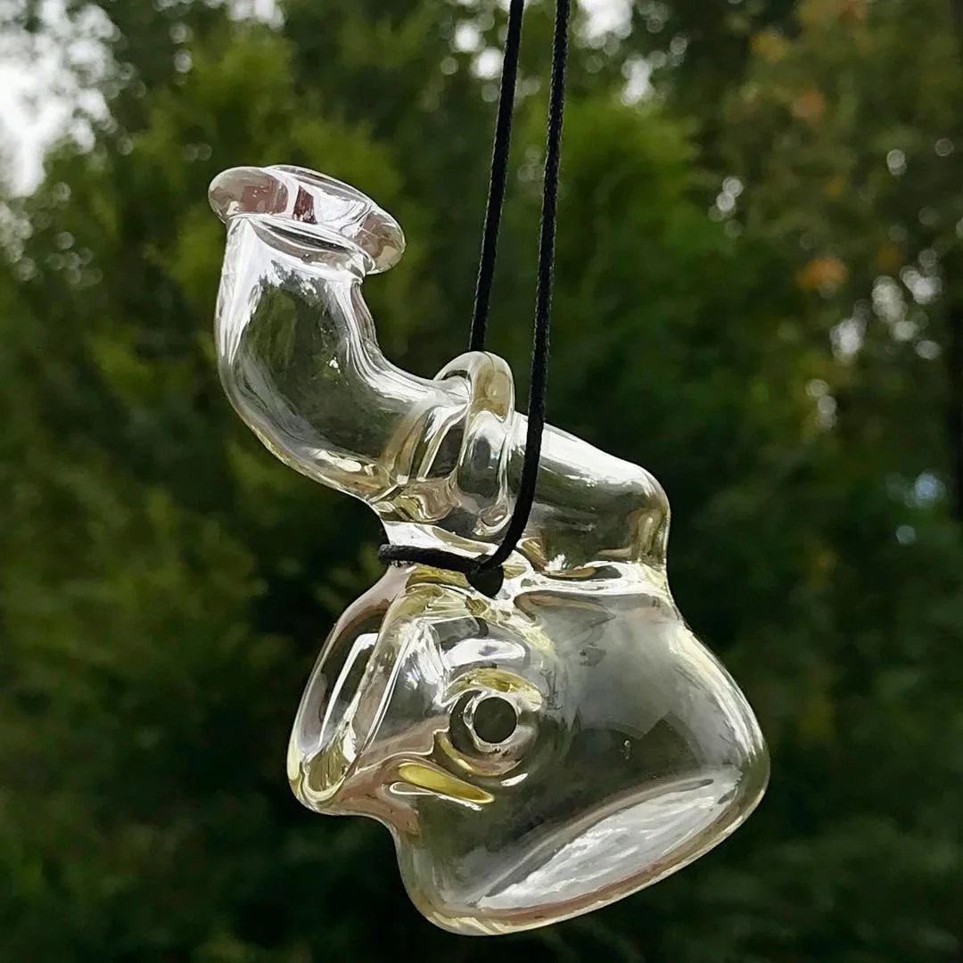 A glass wind chime shaped like a fish hanging outdoors against a blurred green background.