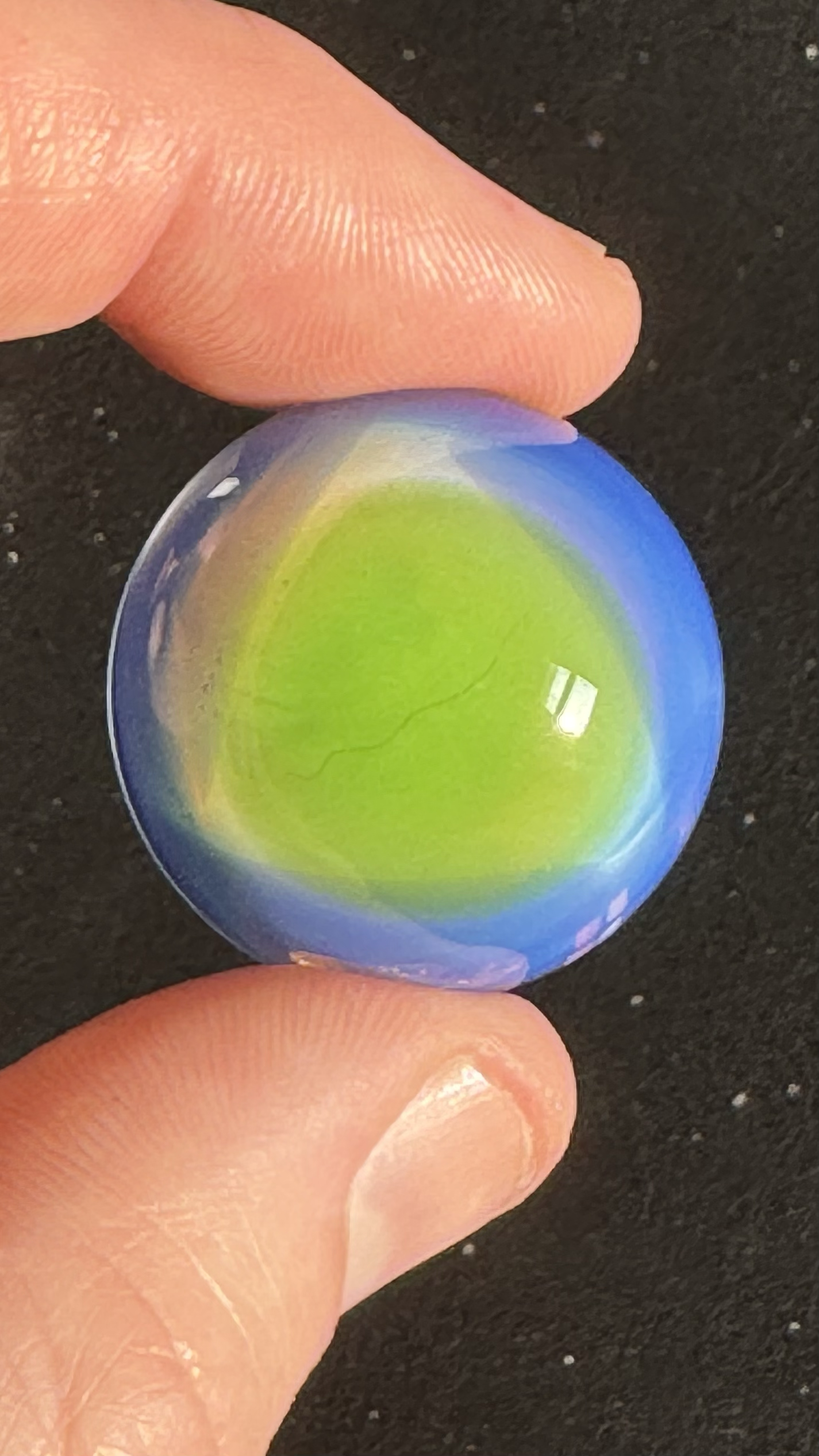 Close-up of a hand holding a multicolored marble with a black background.